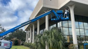 Painter using a boom lift blue to reach high exterior walls of a commercial building