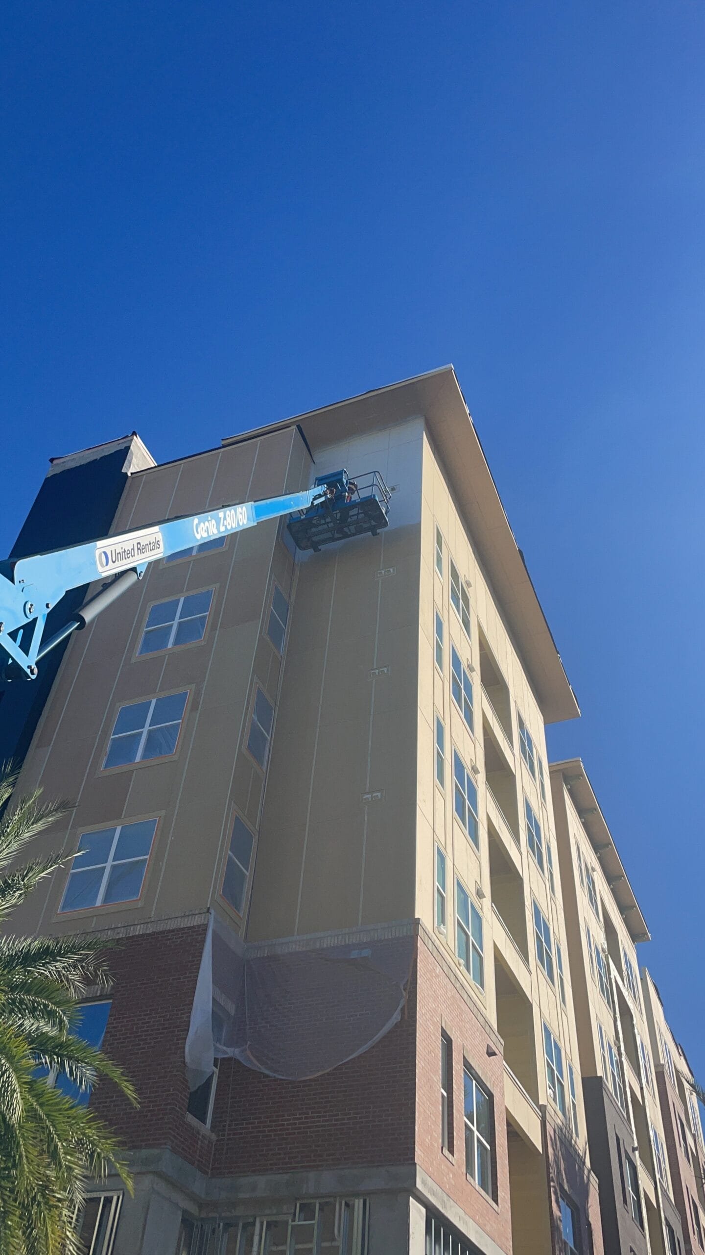 Painter using a boom lift to reach high exterior walls of a commercial building, excellent finish
